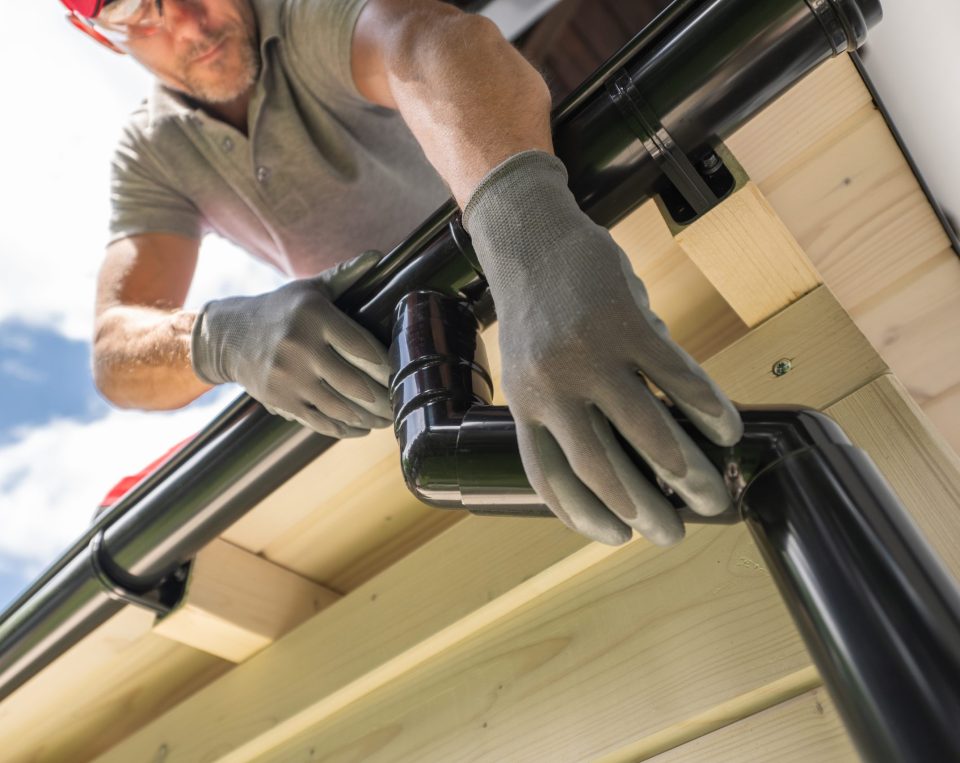 Worker Installing Gutter System on Roof