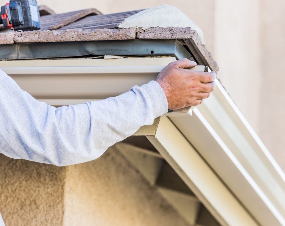 Worker Attaching Aluminum Rain Gutter to Fascia of House.